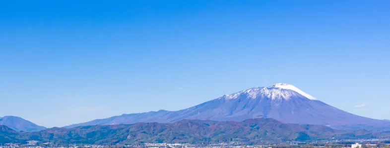 青空の下に広がる街並みと、遠くにそびえる雪化粧の山々。自然と都市が調和した美しい風景。